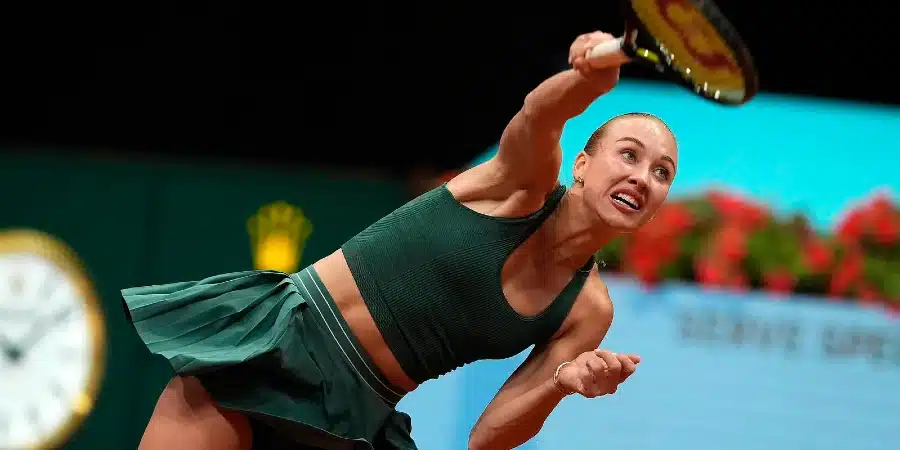 Female tennis player in a green outfit lunges to hit a forehand overhead smash on a tennis court, racket raised mid-swing.