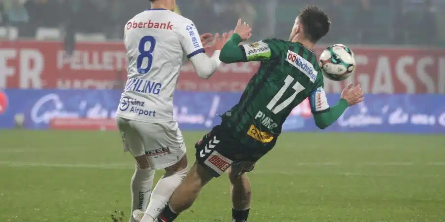 Two soccer players fight for the ball in a rain-soaked match, white kit with number 8 facing a green kit with number 17.