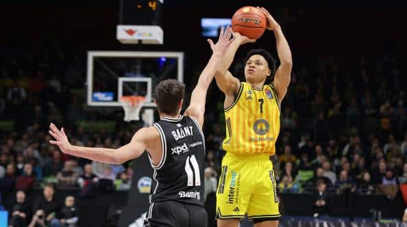 Basketball player in a yellow jersey (number 7) jumps to take a shot over a defender in a black jersey (number 11) during a game.