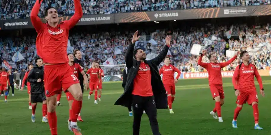 Soccer team in red uniforms celebrates on the field as fans cheer in the stadium.