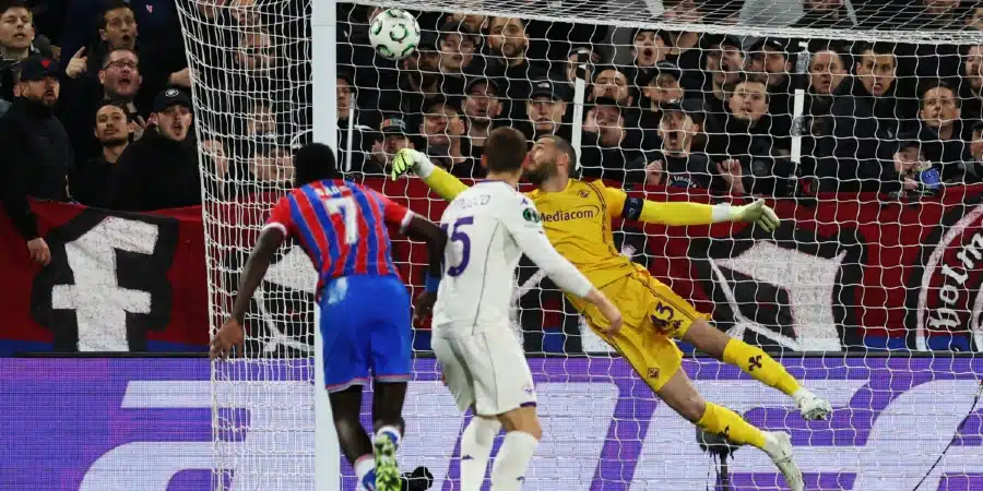 Goalkeeper in yellow dives to block a shot as players contest near the goal in a packed stadium.