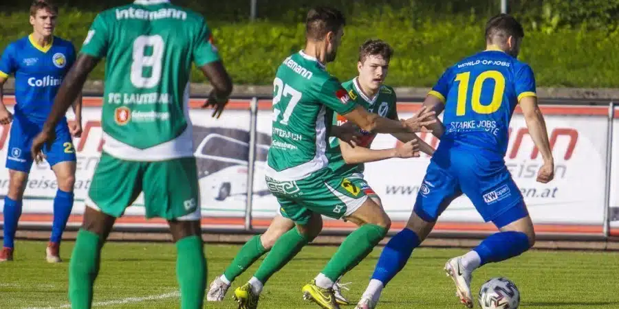 Soccer players in green and blue compete for the ball on a grassy field during a match; blue team player wearing number 10 moves toward the ball.
