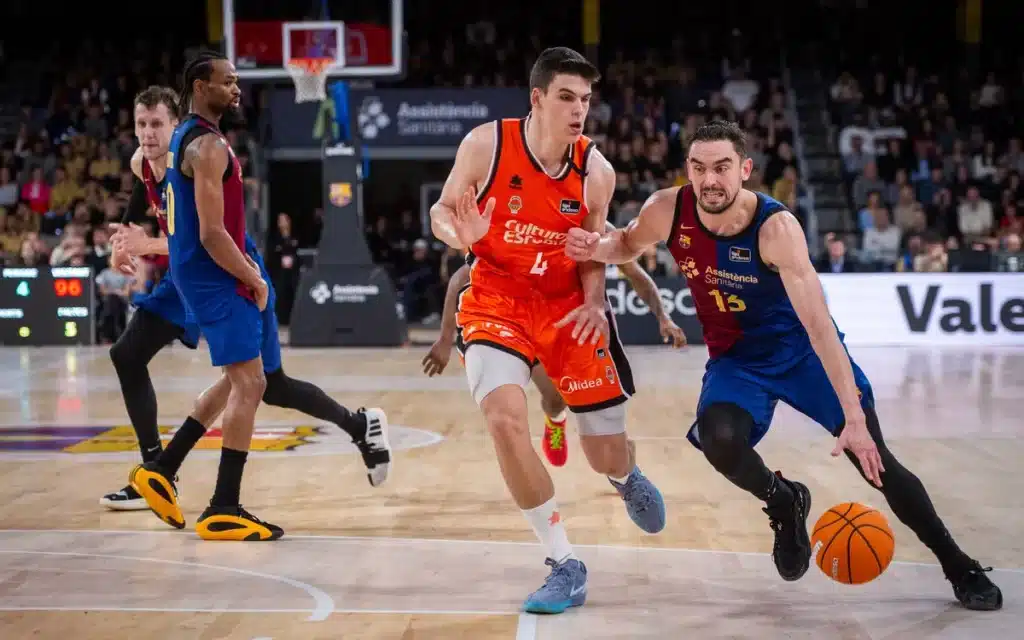 Two basketball players chase a loose ball during a fast break, orange jersey #4 in the lead as a defender in blue blocks from the right.