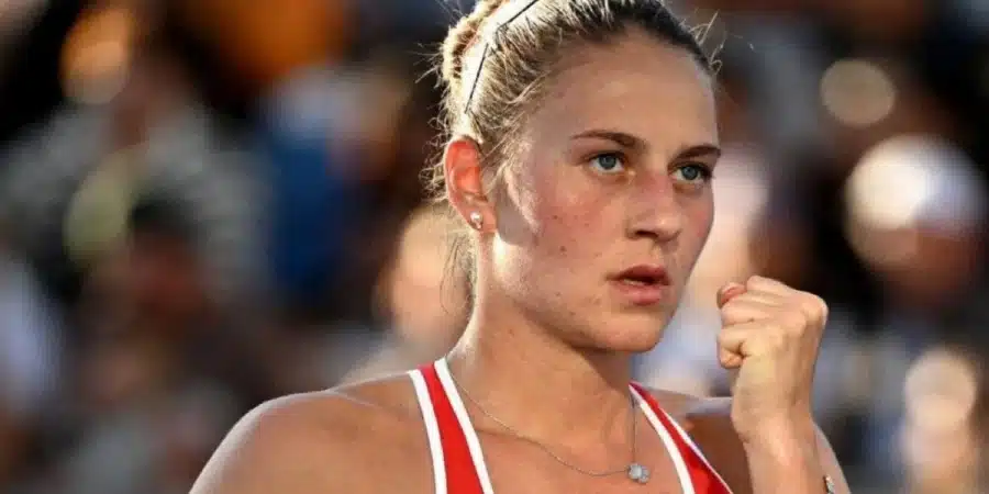 Close-up of a female athlete with a determined expression, fist raised in a victory/cheer gesture during a competition.