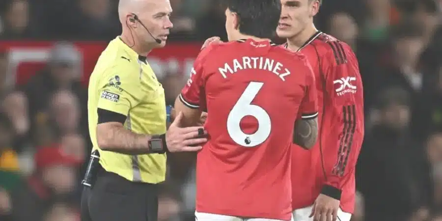 Soccer referee in a yellow kit speaks to two players in red jerseys during a match; one player has 'MARTINEZ' and number 6 on his back.